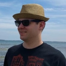 A picture of me, with a hat and sunglasses on, by the seaside